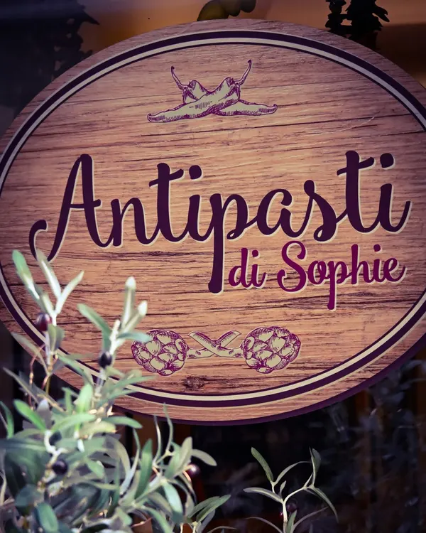 L'enseigne ovale en bois d'Antipasti di Sophie, entourée d'oliviers